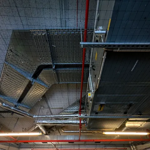 Taubenschutznetz unter einer Tiefgaragendecke, um Kabeltrassen und Sprinklerleitung herum eingefasst